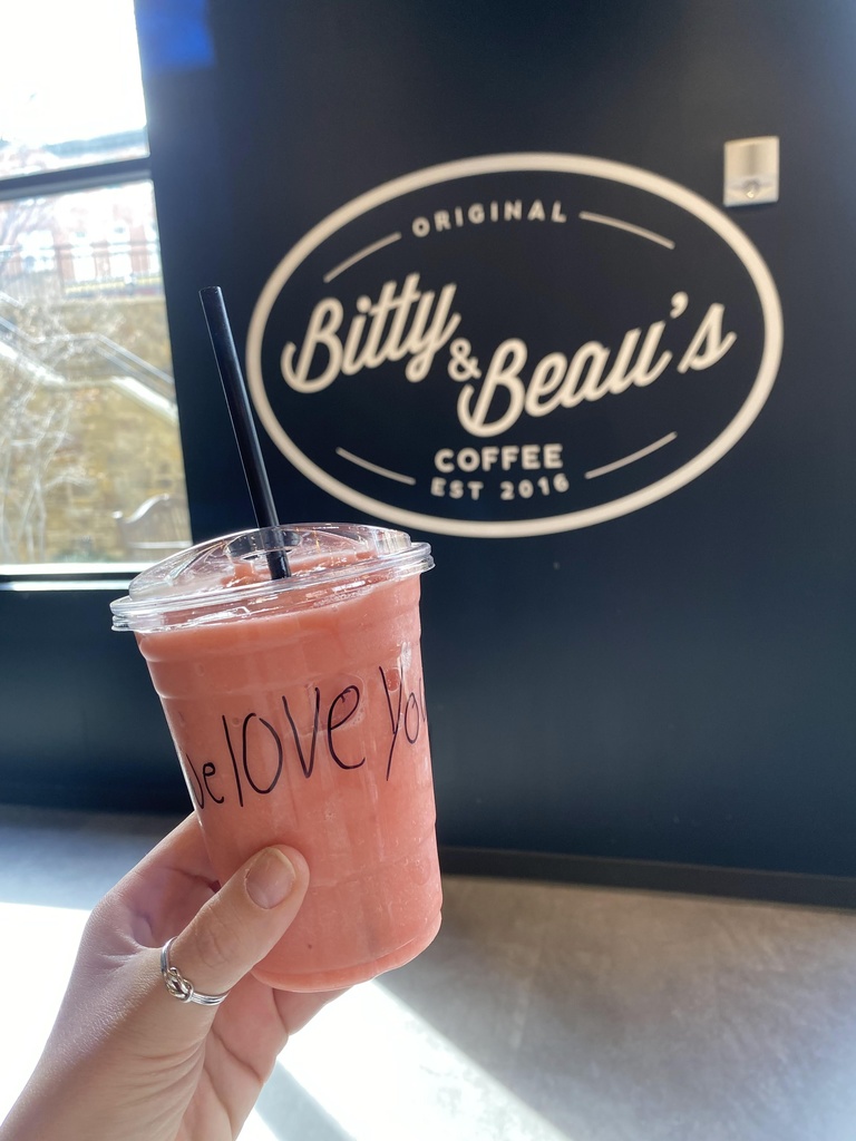 A smoothie in a plastic cup that says 'we love you'. Cup is held in front of the Bitty & Beau's logo.  